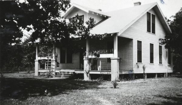 Front view of a farmhouse with rocking chairs on the front porch and trellises leaning against the railings. The house was part of an International Harvester demonstration farm.