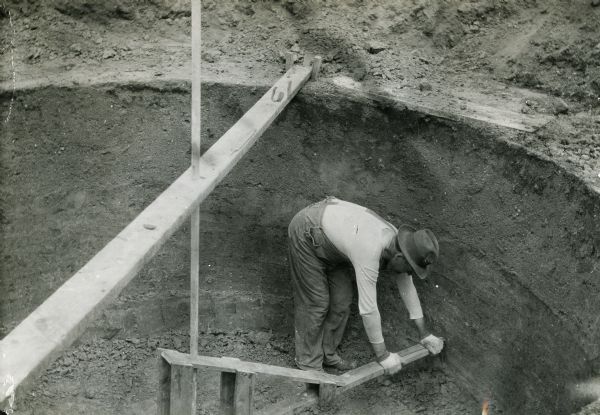 Man working on the construction of the walls for a pit silo. Original caption reads: "J.G. Haney using gauge for smoothing walls of pit silo."