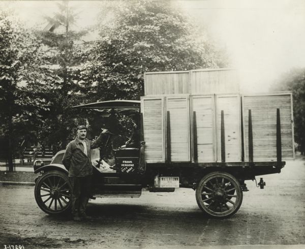 A man is posing standing and holding the steering wheel, and a boy is sitting in the passenger seat of an International Model F (or 31) truck operated by Frank Vergenz's City Dray (hauling business).