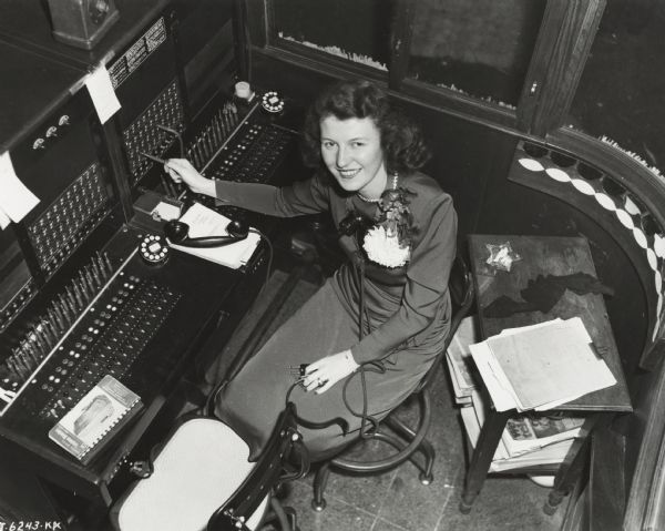 Original caption reads: "Marie McCaddin, New York branch telephone operator." Overhead view of woman sitting at a switchboard.
