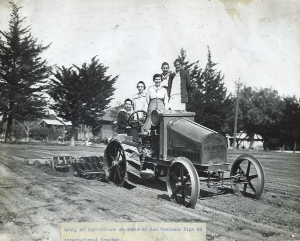 A group of female agriculture students at San Fernando High pose on an International 8-16 tractor. Stenciling is on the front of the tractor.