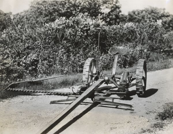 Front view of a McCormick-Deering mower on dirt road with decal below seat.