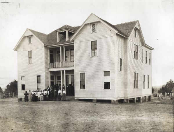 View across yard of a group of African American students from the North Alabama Baptist Academy gathered on the building's front steps for an outdoor group portrait.