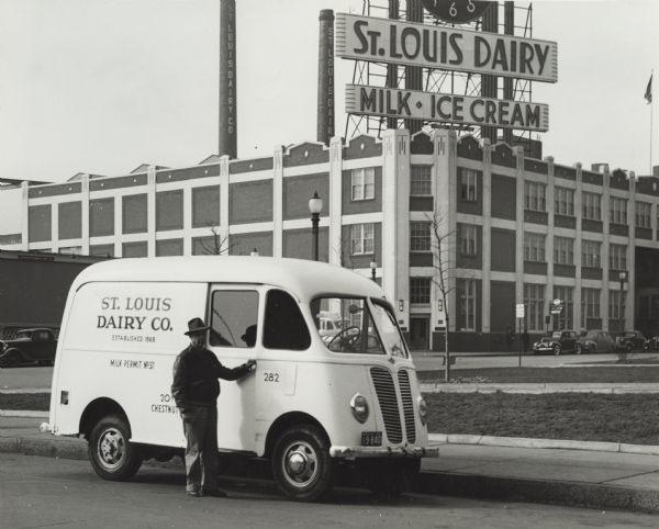 A man is standing beside International Metro delivery van used by St. Louis Dairy parked outside company factory. A sign on the dairy building reads: "St. Louis Dairy / Milk / Ice Cream."
