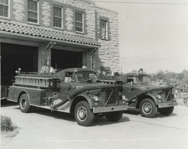 Two International Model V-206 fire trucks parked outside a fire station. There are men sitting inside the trucks, and "Jefferson City" is painted on the front hoods.