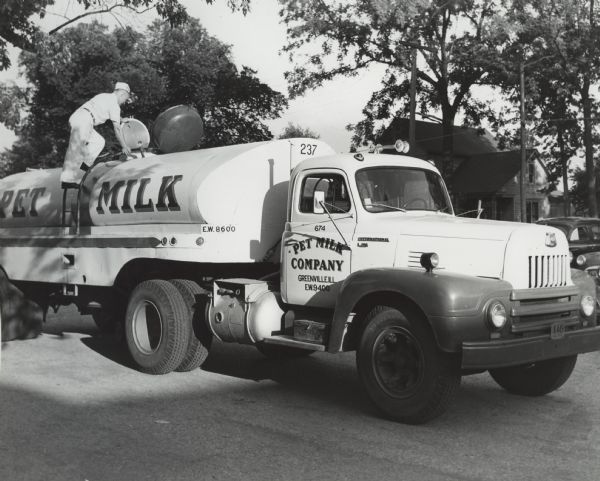 A truck driver inspecting the tank of his International L-190 truck. The truck was owned by the "Pet Milk Company."