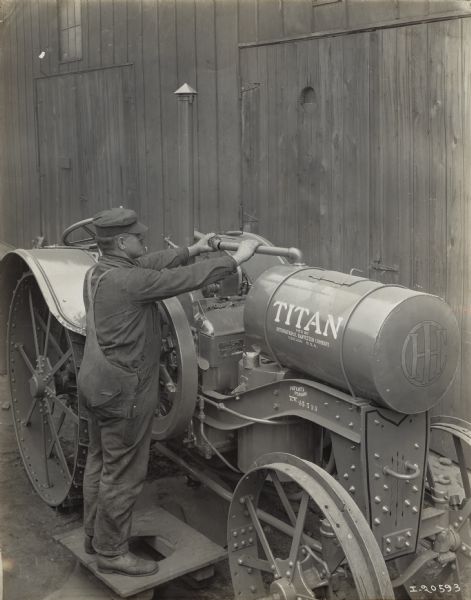 Man wearing overalls and cap is standing near a Titan 10-20 tractor. Decals and/or stencils are on the tractor.