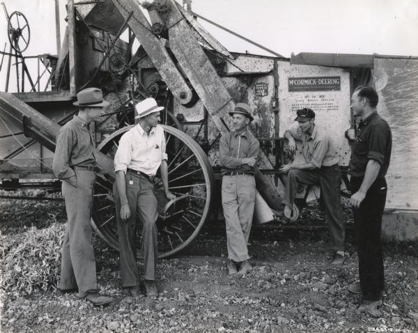 Five men gathered near a McCormick-Deering No. 31 Harvester Thresher. Decal and stenciling are visible. Original caption reads "No. 31 BW West Coast Special Harvester Thresher with pick-up attachment pulled by F-20 Farmall in baby lima beans. Owned by R.C. Anderson, Vernalis, California, who operates 700 acre farm and last year harvested 1,700 acres of flax with his new 31-RW and probably 700-800 acres of beans. Shown on farm owned by Glenn Allard, who had 200 acres in beans . . . left to right are shown G.M. Conway, blockman, San Francisco general line branch; W.E. Lyons of Lyons Implement Company, Tracy, California; R.C Anderson (see above), and Floyd Davis and L.C. Simmons, Service men employed by Mr. Lyons."