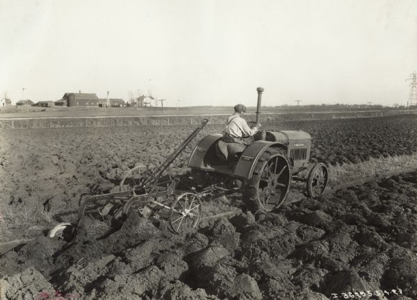 Three-quarter rear view of man pulling a P&O (Parlin and Orendorff) Little Wonder plow with a McCormick-Deering 10-20 tractor. Decals are on the tractor and the plow.