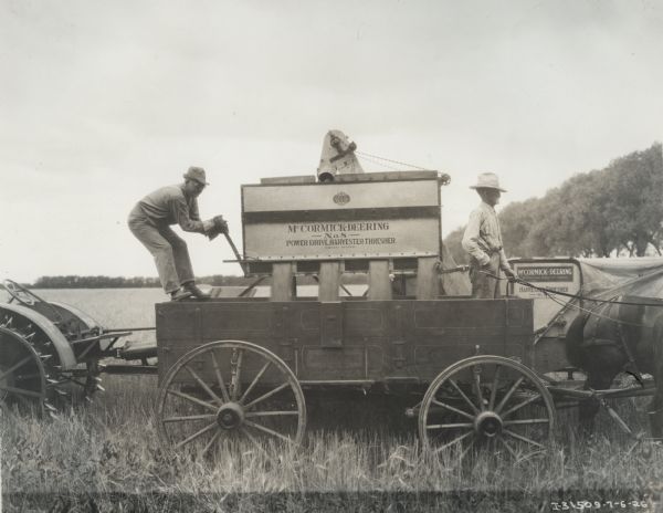 Two men working with a McCormick-Deering Power Drive harvester-thresher (combine) in a field. Decals and/or stencils are on the machine.