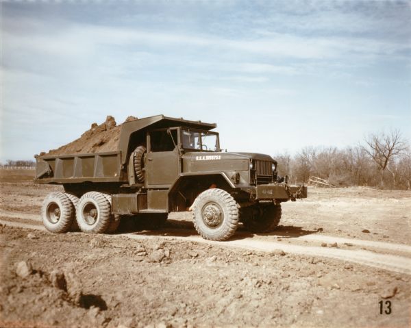Color photograph of an engineer construction battalion with an M-51 dump truck. The battalion used the truck to transport topsoil along a dirt road at Fort Hood. The specifications of the M-51 are as follows: 167" WB Truck, Cargo, with 14:00 x 20 front & single rear tires.