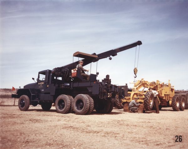 View towards men using an M-62 wrecker to lift a piece of construction equipment. The specifications of the M-62 are as follows: 179" WB Truck, Medium Wrecker, with 11.00 x 20 front & dual rear tires.