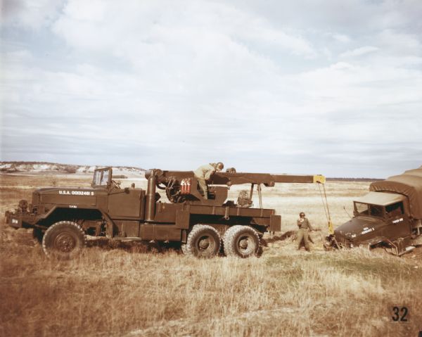 Color photograph of members of the 73rd Armored Field Artillery using an M-62 wrecker to remove a damaged truck from a field at Fort Hood. The specifications of the M-62 are as follows: 179" WB Truck, Medium Wrecker, with 11.00 x 20 front & dual rear tires.