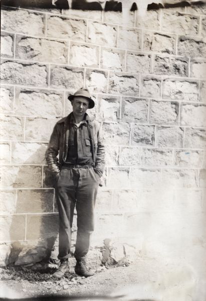 Mr. Schlosser, superintendent of the Oak Lake, Manitoba, Canada demonstration farm, poses for a portrait while standing against a stone wall or building.