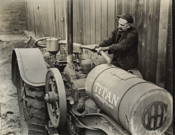 Three-quarter front view of a Titan 10-20 tractor. A man wearing a hat is filling the tank. Stencils and/or decals are on the tractor.