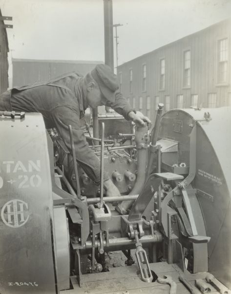 Rear view of a Titan 10-20 tractor mid-repair. A man wearing overalls and a hat is working on the tractor. Stencils and/or decals are visible on the tractor.