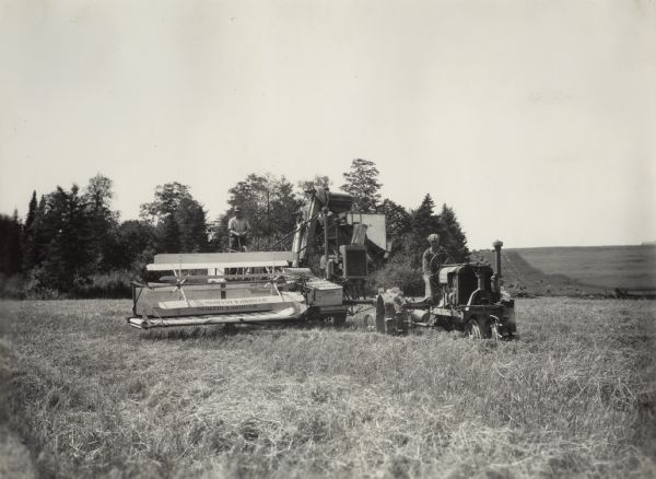 Man on a Farmall tractor, pulling a McCormick-Deering harvester-thresher (combine) in a field. Original handwritten caption says: "Taken on farm of G.N. Cochron, Caribou Maine. Mr. Cochron on thresher." Small decals on the combine read: "Important Keep Feeder Chain Tight" and "Always Stop Engine Before On Or Near Moving Parts."