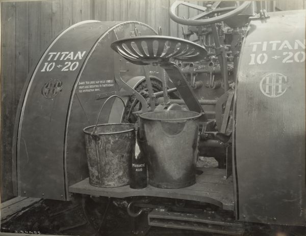 Rear view of Titan 10-20 tractor showing stencils and/or decals. Two metal buckets are behind the seat, as well as a bottle marked "Muriatic Acid".