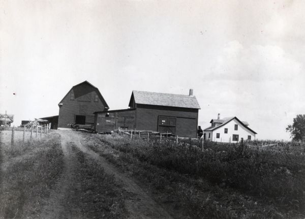 View of an International Harvester Company demonstration farm, taken from a dirt road facing east, towards several barns and a farmhouse.