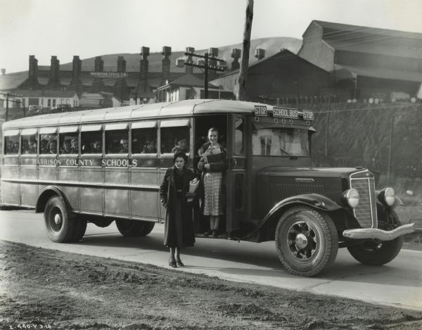 Students aboard International Model C-50 school bus used by Harrison County schools. Two female students are standing near the bus.