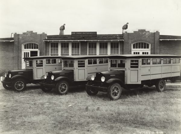 Three International school buses parked in yard outside school building. A sign on the roof reads: "Fox Consolidated School".