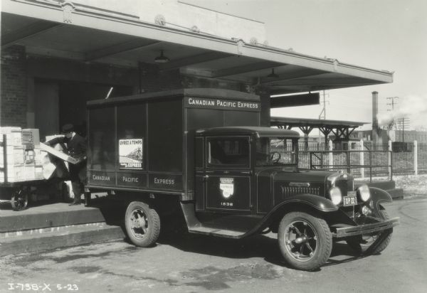 Man loading Canadian Pacific Express delivery truck at a depot loading dock. In the background are industrial buildings.