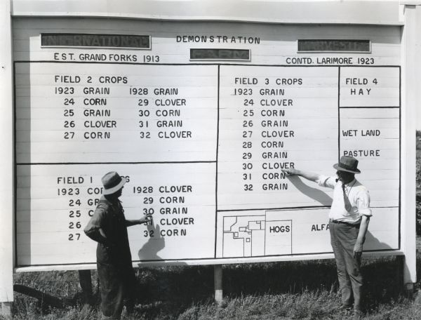 John Haney and Joe Clark look at a board detailing a crop rotation plan at an International Harvester demonstration farm.