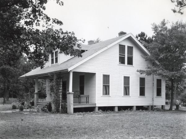 Exterior view of a farmhouse on an International Harvester demonstration farm. Two swings are hanging from the ceiling on the front porch of the house.