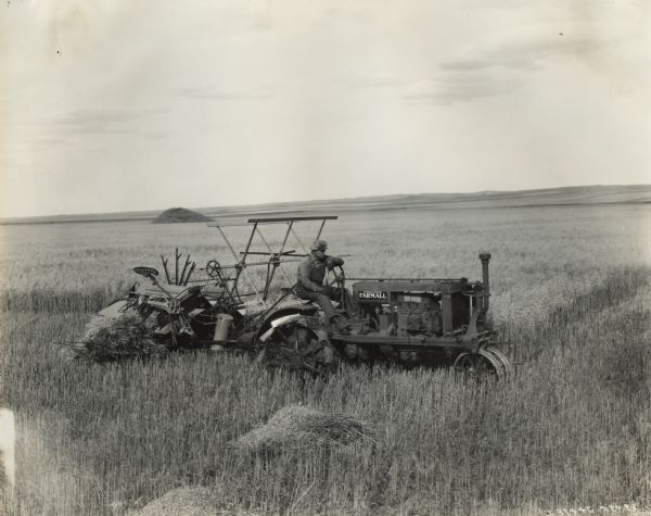 A man is using a Farmall Regular tractor and a grain binder to harvest a field crop on an International Harvester Company demonstration farm in Gull Lake, Saskatchewan, Canada.