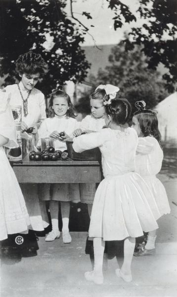 Mrs. Marie Cromer Zigler, left, assisting a group of girls as they gather around a table to participate in a girls' Canning Club.