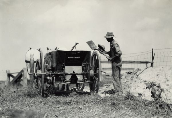 Two men with shovels work with a horse-drawn McCormick-Deering lime spreader. Decals are on the lime spreader.