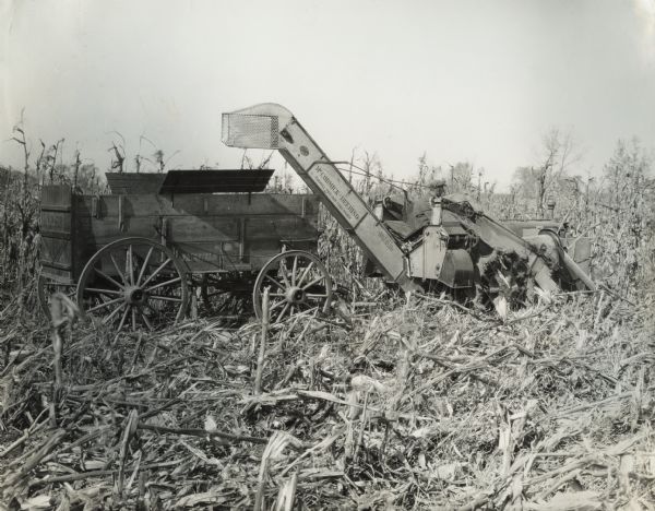 Man operating a McCormick-Deering two-row corn picker in field. Stencils and/or decals are on the machine.