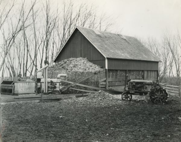 McCormick-Deering No.2 corn sheller and Farmall Regular tractor on Dick Wormley's farm. A man stands on the left gathering the shelled corn into a "utility hog feeder" manufactured by W. A. McCollough and Sons.
