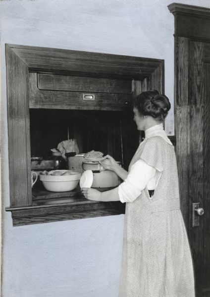 Mrs. John Bowers removing a plate of food from the dumbwaiter in her Benton County farmhouse.