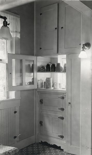 Jars of food are stored in an opened cabinet within a farmhouse kitchen.