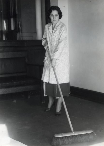 Irma Evans using a broom to sweep the floor near a wooden bench.