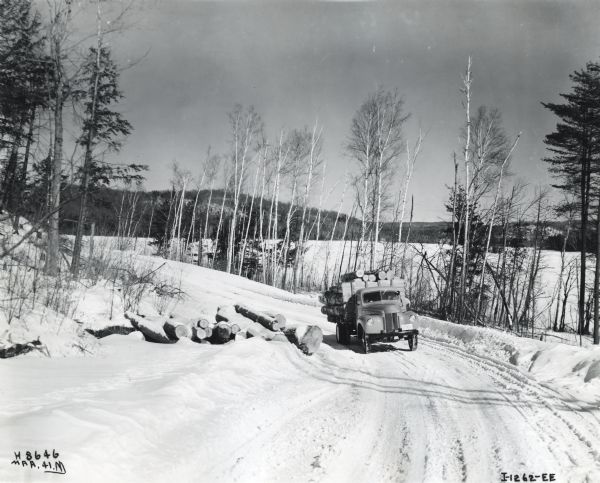 An International K-5 truck drives on a snow-covered hillside road in Eagle Lake, Ontario, Canada to deliver cut logs.