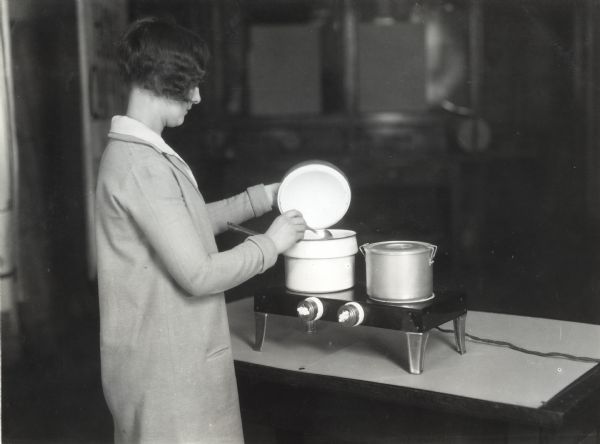 A woman mixing food in a pot heated on an electric plate.