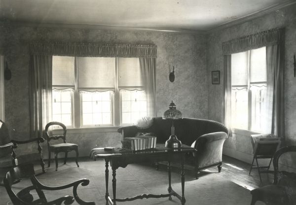 A couch, several wooden chairs, and a table are arranged in the living room of Mrs. Sam Barns.