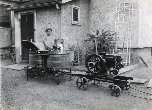 Woman washing clothes outdoors with a Dexter washing machine powered by a stationary McCormick-Deering 1 1/2 horsepower type "M" engine. Photograph taken at the home of William Holtzhuetter for International Harvester's Agricultural Extension Department.