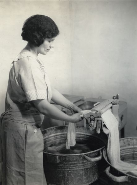 Mrs. Granere using a Maytag wringer and two metal rinsing buckets to wash clothing on the International Harvester demonstration farm.