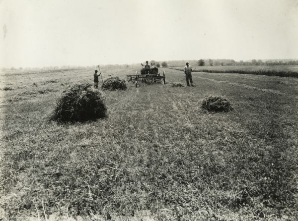 Two men work in a field, and another man drives a team of horses pulling a hay rake. Original caption reads: "Demonstration farms. Alfalfa, with and without 400 lbs per acre of acid-phosphate."