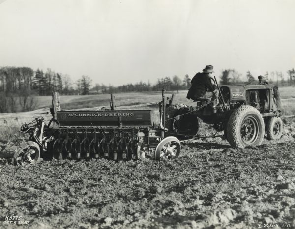 A man uses a Farmall F-30 tractor to pull a harrow plow with a McCormick-Deering drill attachment. This attachment allowed for one step tilling and seeding.