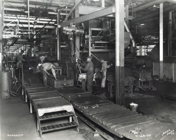 Factory workers at International Harvester's Indianapolis Truck Engine Works complete work on the drag half of molds on the mold conveyor.