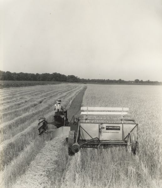 Elevated view of a man using a Farmall tractor to pull a McCormick-Deering windrow harvester in a field of rye. Original caption reads: "Elliot A. Pritchard, Waterman, Illinois. 8' Windrow in rye."