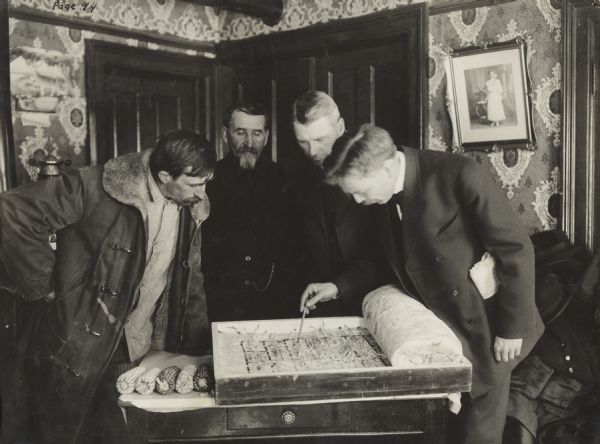 Four men gathered over agriculture work. Original caption reads: "Assistant County Superintendent Calley explaining corn testing work to the school directors."