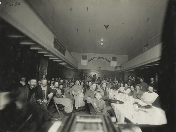Group gathered in the gymnasium of the Woldale Rural School for a Christmas "hobo" party. Attendees are dressed as "hobos." The original caption notes that "this gymnasium is [in] constant use for social gatherings."
