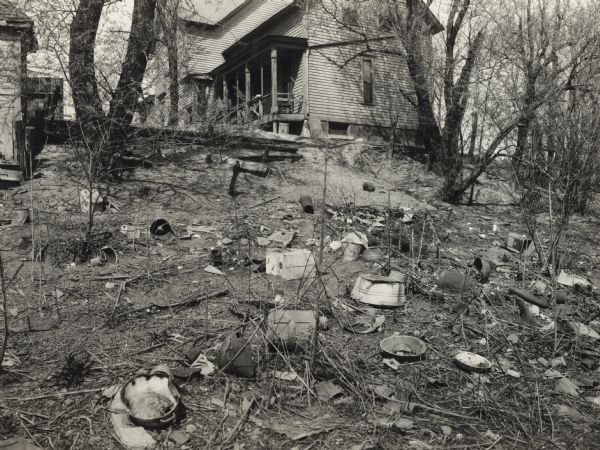 Debris-strewn back yard of a farmhouse. Original caption reads: "Farm buildings - cluttered up back yard at John Eshe farm."