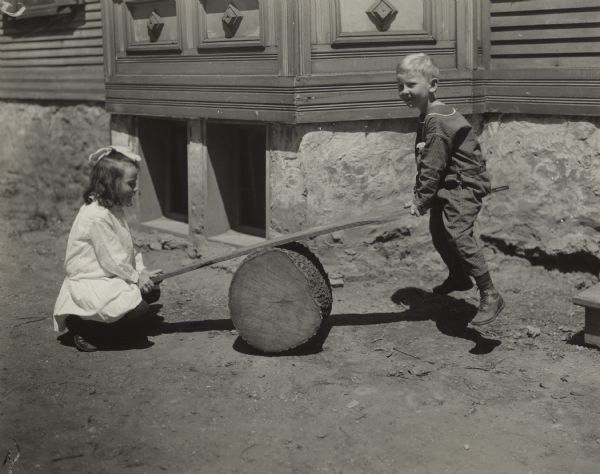 Young boy and girl playing on a makeshift teeter totter made from a board and a section of a log. The children are likely playing near Sunnyside School.