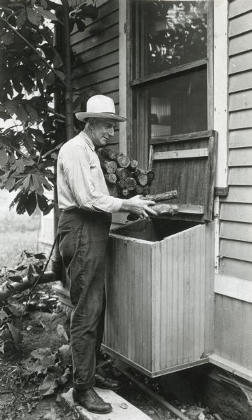 A man placing logs inside a woodbox attached to a house.